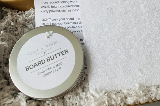 Round tin of Board Butter for Chopping Board Conditioning Kit on shredded paper with partially visible instructions.