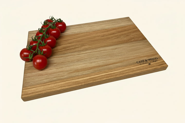 A medium-sized solid oak chopping board with a knife on it, displayed on a beige surface, with cherry tomatoes to the side.